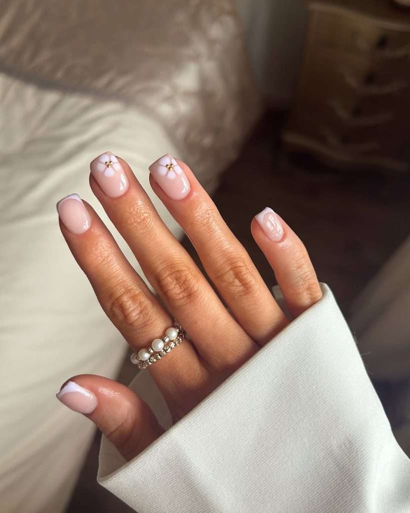 Short square nails with sheer pink base and minimalist white flower accents with gold centers

