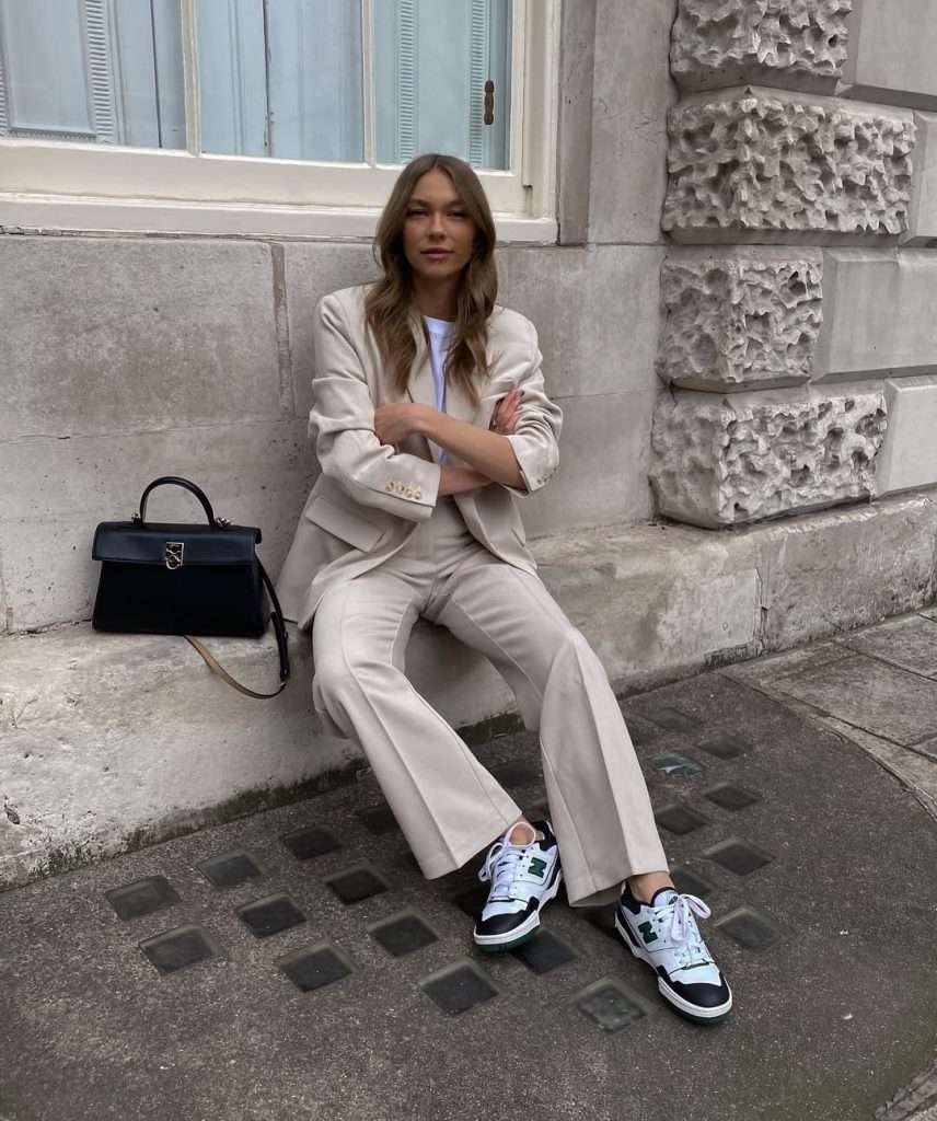 Business casual outfit with cream blazer, white t-shirt, matching cream trousers, black and white sneakers and black structured handbag