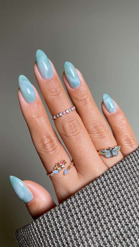 Long almond nails with light blue marbled design with white swirls
