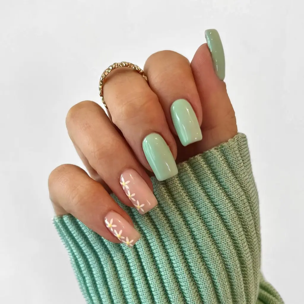 Square nails with sage green polish on some nails and transparent pink base with white daisy flower designs on others
