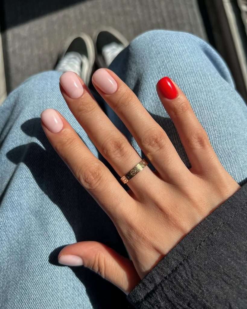 Short square nails with light pink polish and one bright red accent nail
