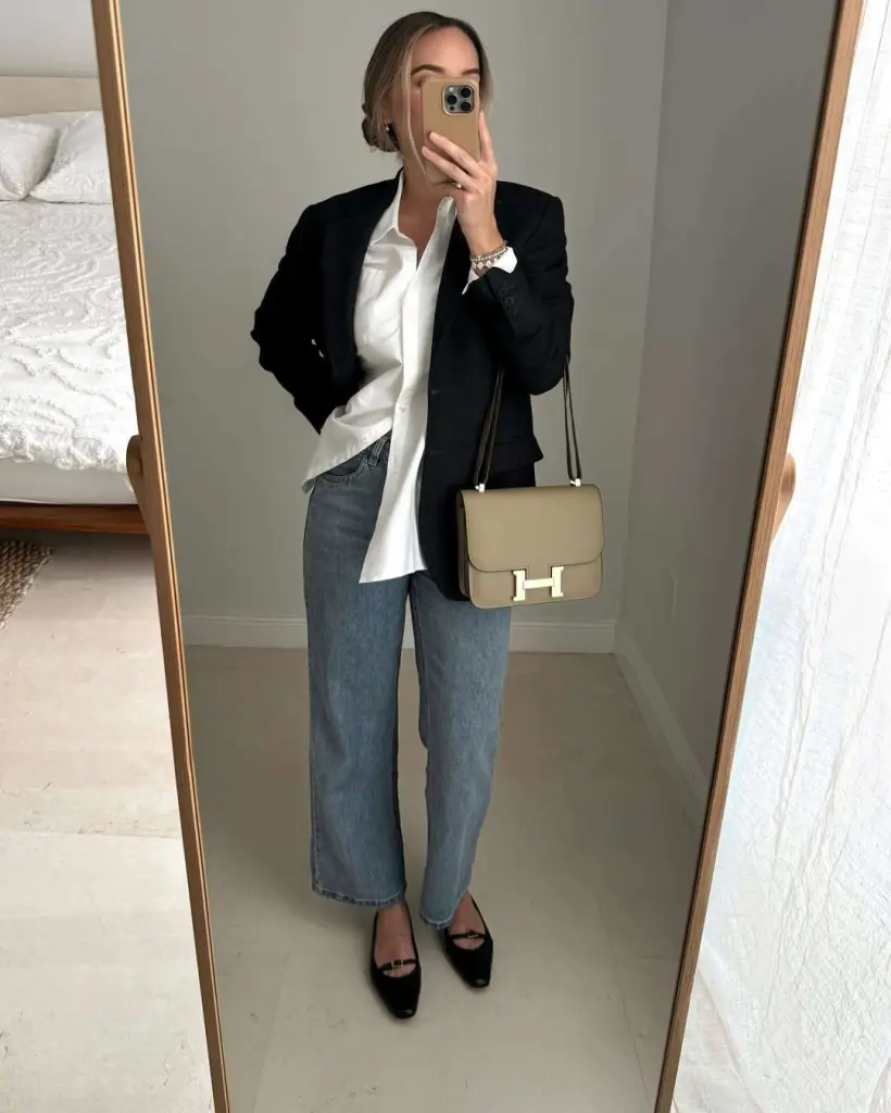 Business casual outfit with black blazer, white oversized button-down shirt, blue straight-leg jeans, black flats and beige designer shoulder 
