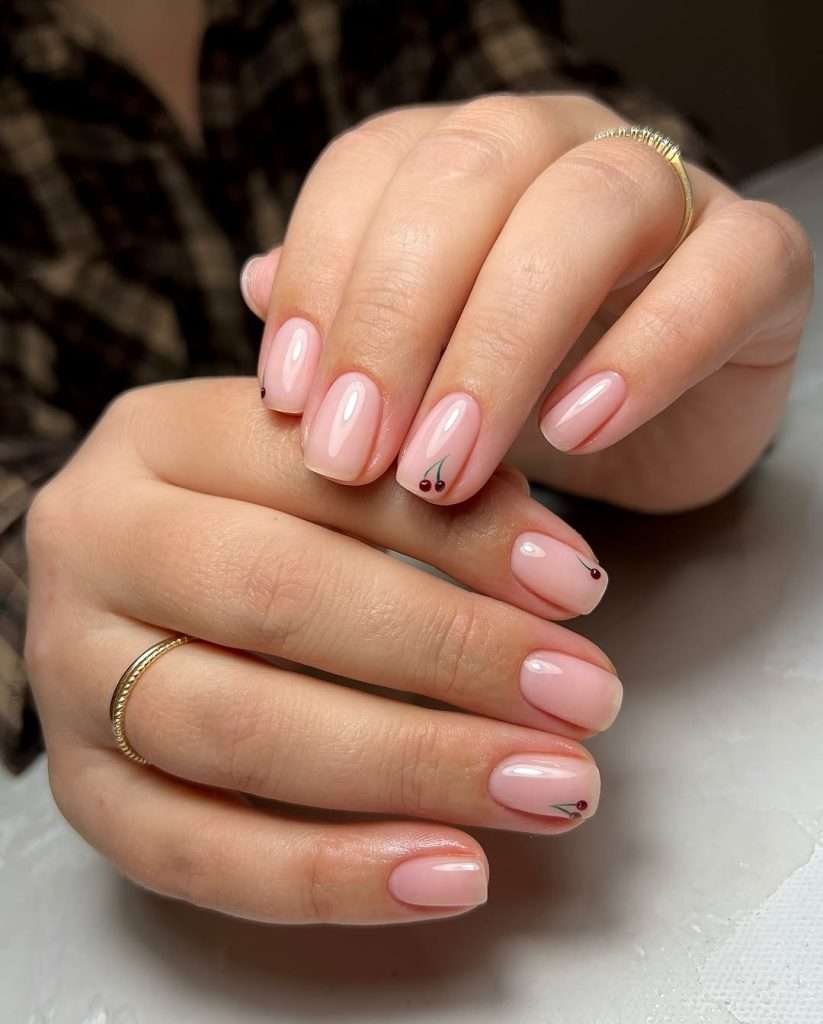 Short square nails with sheer pink polish and small cherry designs on accent nails