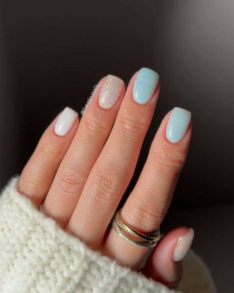 Short square nails alternating between white and light blue polish, with one sparkly glitter accent nail