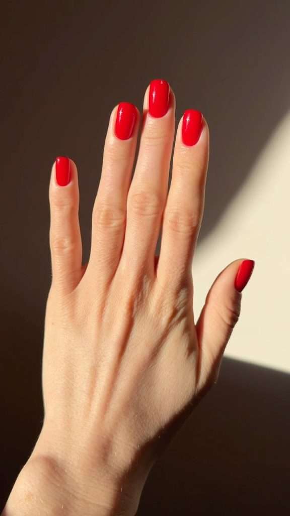 Short square nails painted in glossy bright red polish
