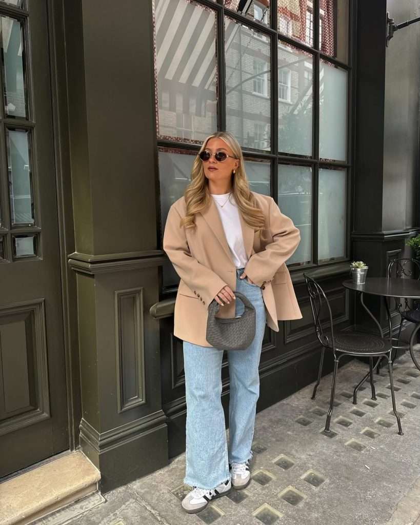  spring outfit with camel oversized blazer, white t-shirt, light wash wide leg jeans, white and black sneakers and gray woven shoulder bag