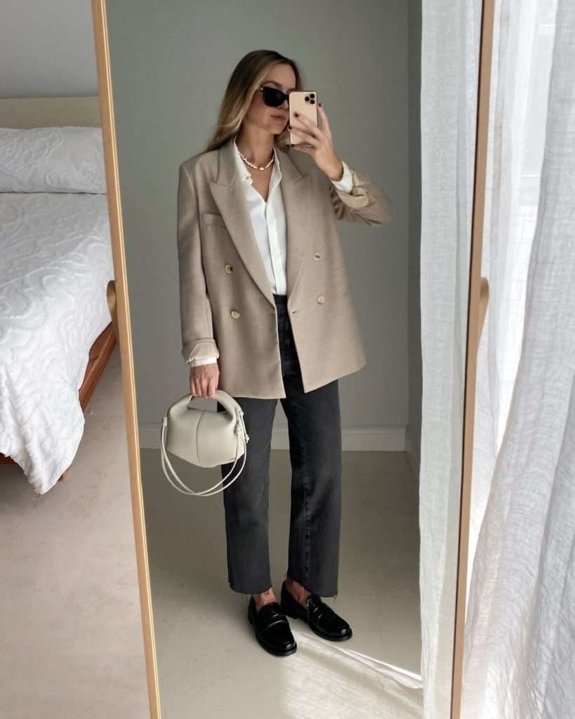 Business casual outfit with beige oversized blazer, white button-up shirt, dark grey straight-leg jeans, black loafers, pearl necklace and small cream handbag