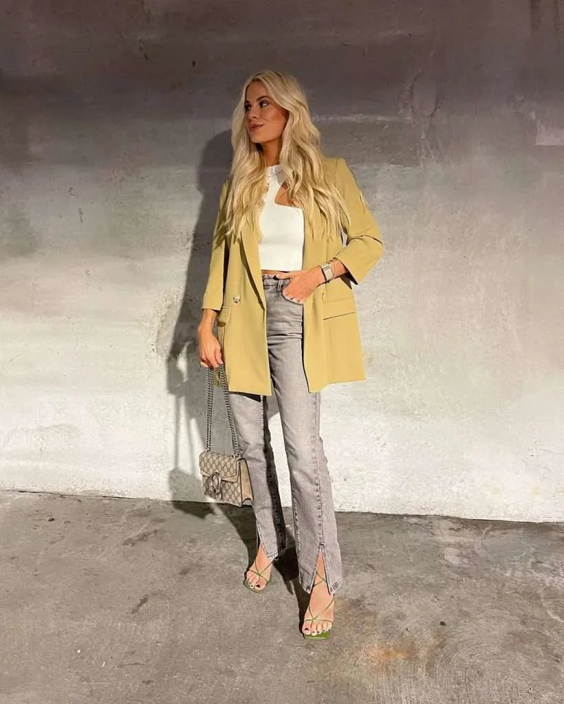 Classy spring outfit with oversized pastel yellow blazer, distressed light wash straight leg jeans, nude strappy heeled sandals, and beige monogram print shoulder bag