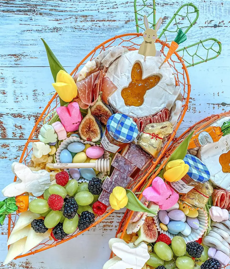 Easter-themed charcuterie basket filled with fresh berries, chocolate bunnies, Peeps marshmallows, cheese, prosciutto, figs, and bunny-shaped jam on a rustic blue background