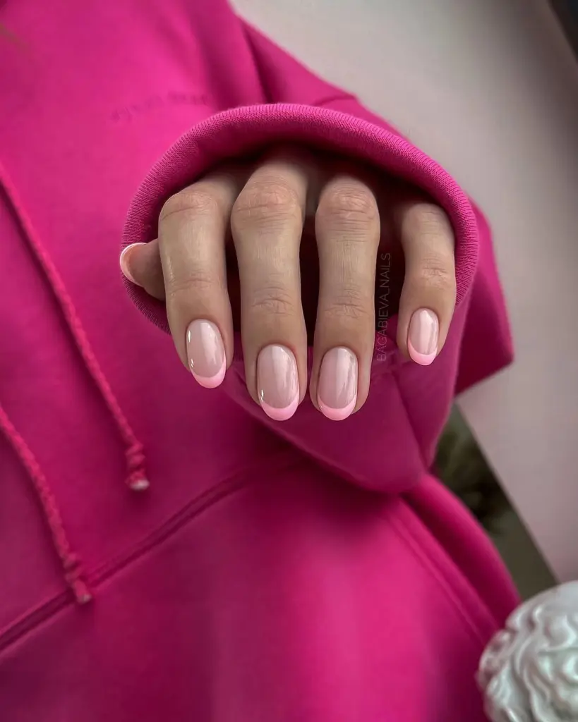 Short oval glossy nails with transparent nude base and thin pink French tips, offering a minimalist spring elegance
