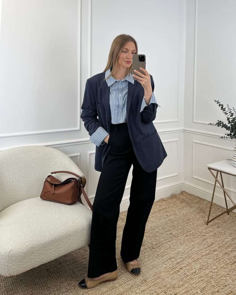 Business casual outfit with navy blazer, blue striped button-up shirt, black wide-leg trousers, tan and black cap-toe flats and brown leather shoulder bag
