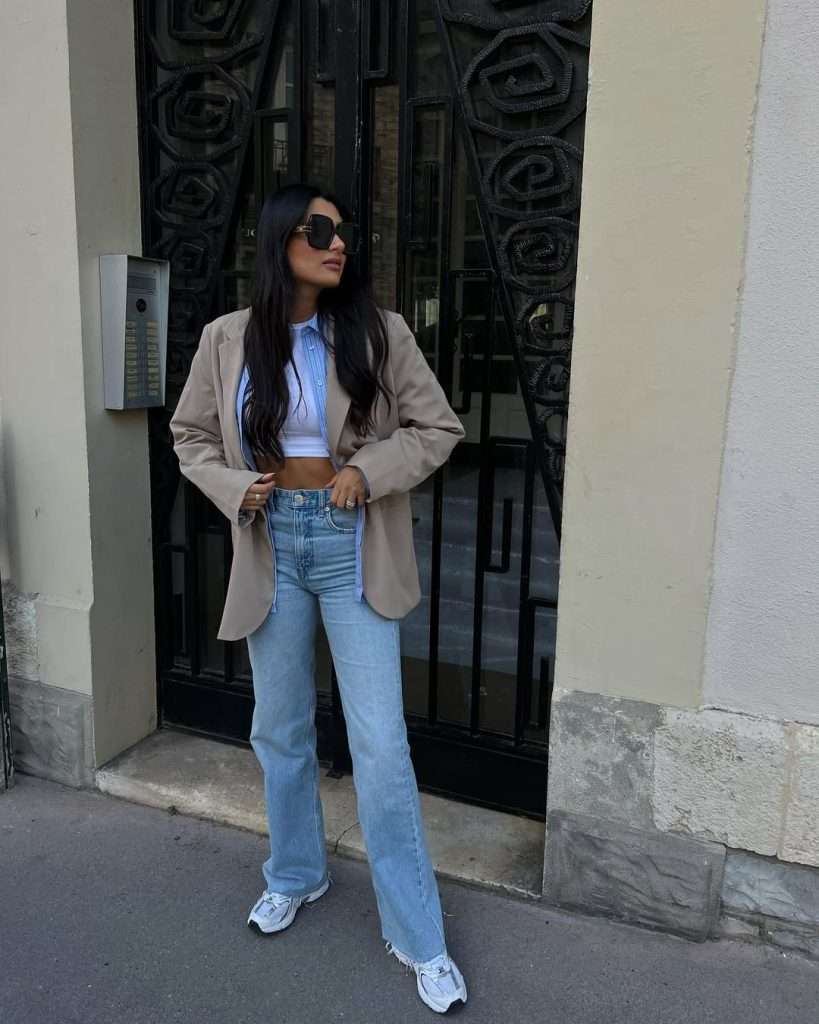 Casual spring outfit with beige oversized blazer, light blue button-down shirt, white crop top, straight leg jeans and gray New Balance sneakers