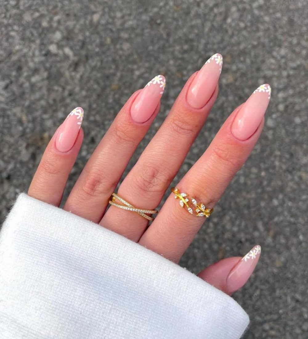 Almond-shaped pink nails with delicate white daisy flowers painted at the tips, creating a fresh spring French manicure