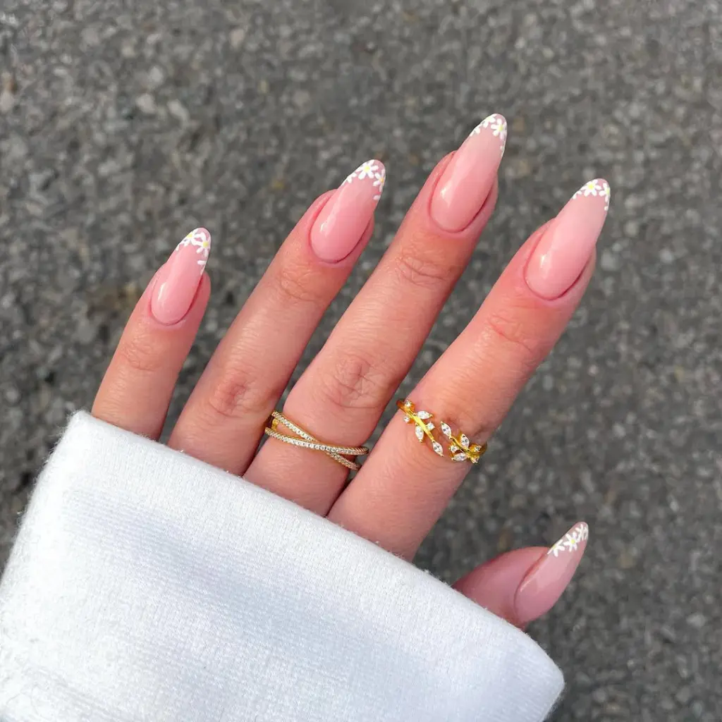 Almond-shaped pink nails with delicate white daisy flowers painted at the tips, creating a fresh spring French manicure
