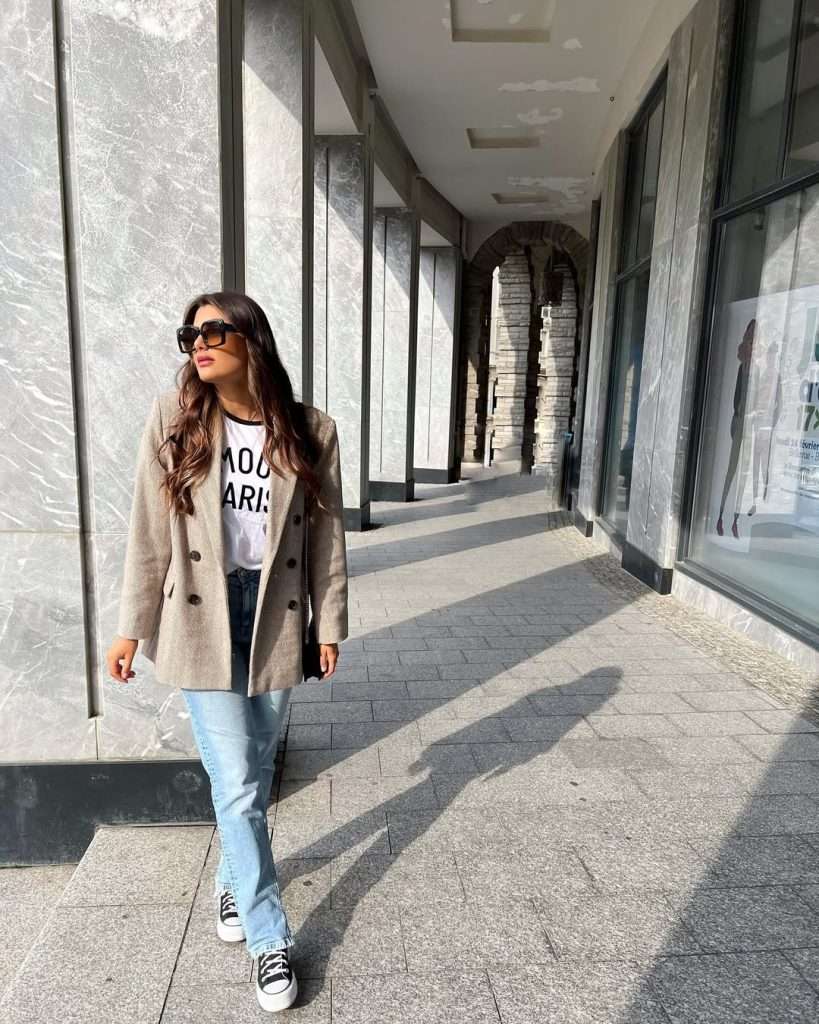 Casual spring outfit with beige oversized blazer, white graphic t-shirt, light wash straight leg jeans and black Converse sneakers