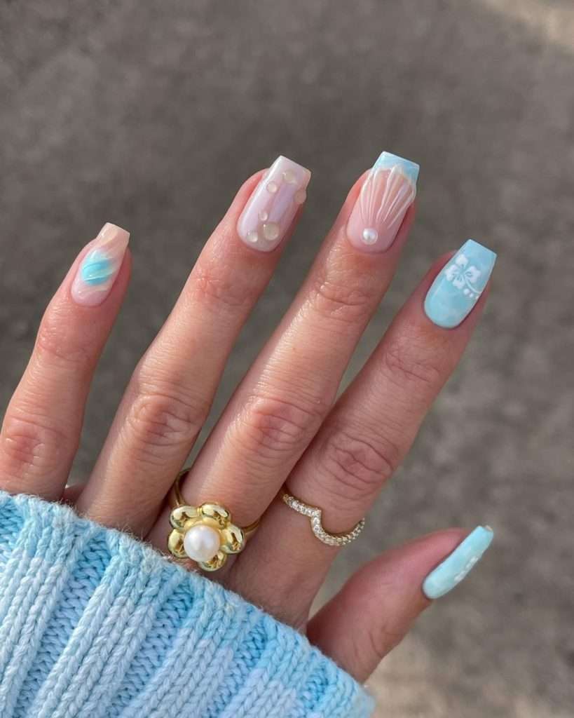 Long square nails with blue and sheer pink, seashell designs, pearl decorations and hibiscus flower accent