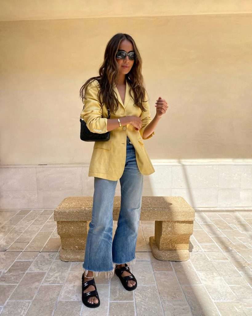 Sunny spring outfit with pastel yellow blazer, light wash wide leg jeans, black Chanel sandals and black quilted shoulder bag
