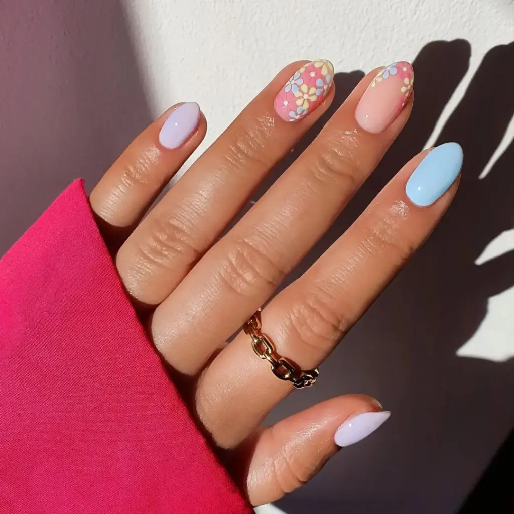 Short oval nails with pink and white base featuring pastel blue, yellow and pink flower accents in confetti pattern