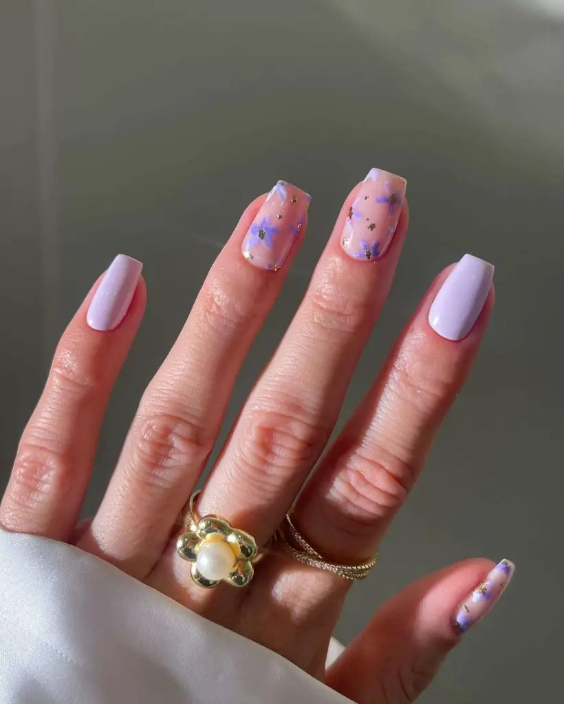 Medium squoval nails with lilac flowers on sheer pink base and gold flake accents
