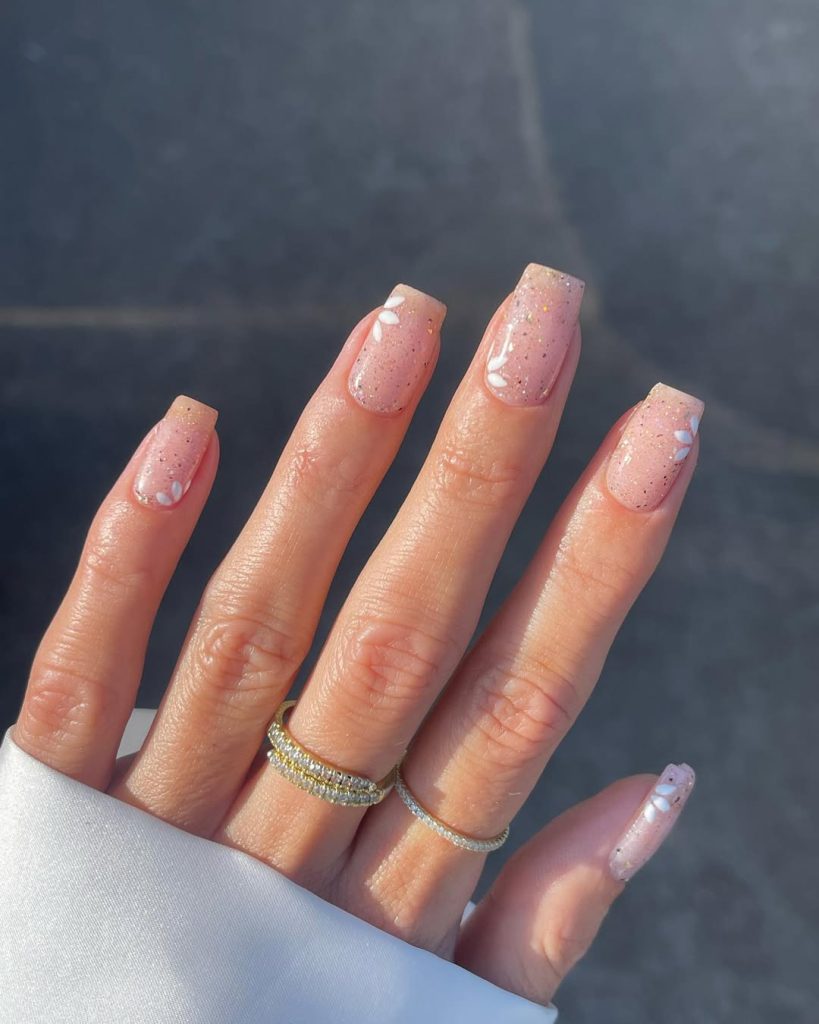 Square pink glitter nails with white daisy flower accents and gold sparkle details