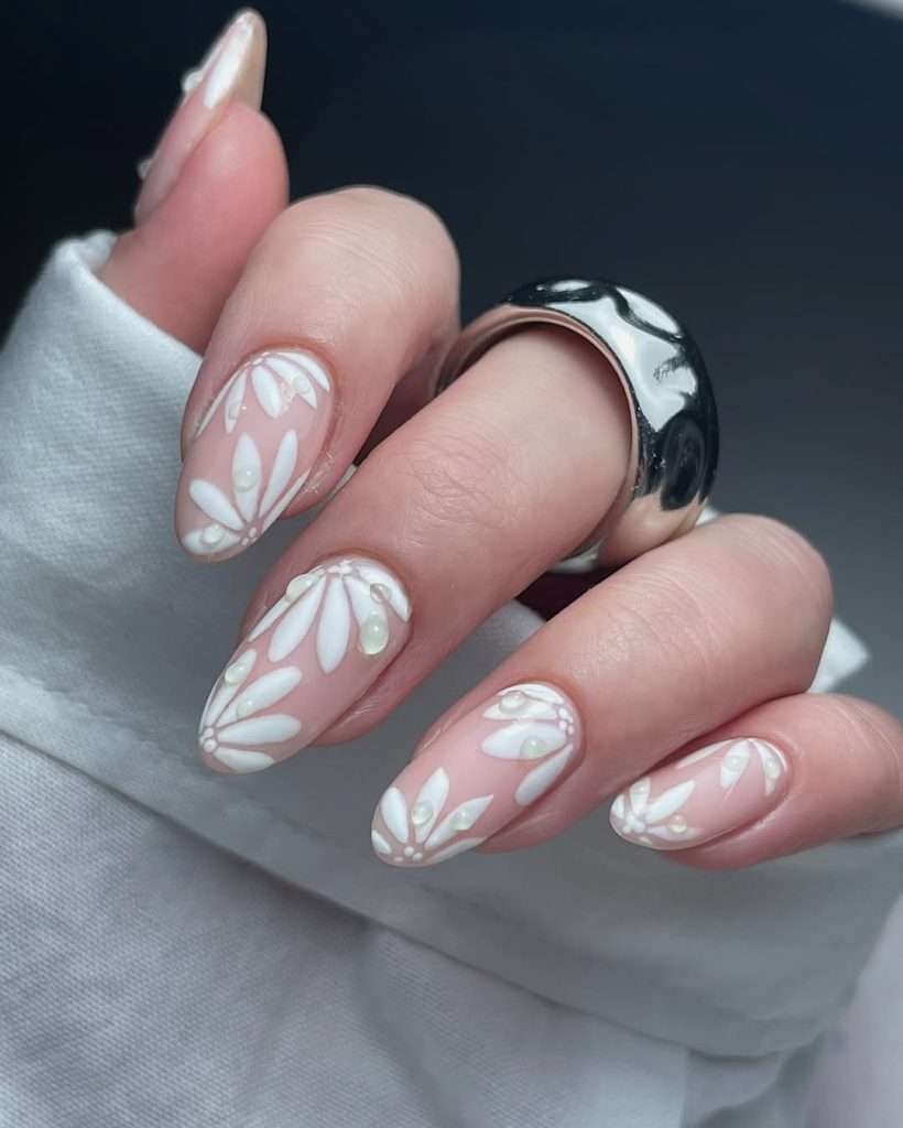 Long almond nails with nude base, white daisy flower designs and pearl decorations 