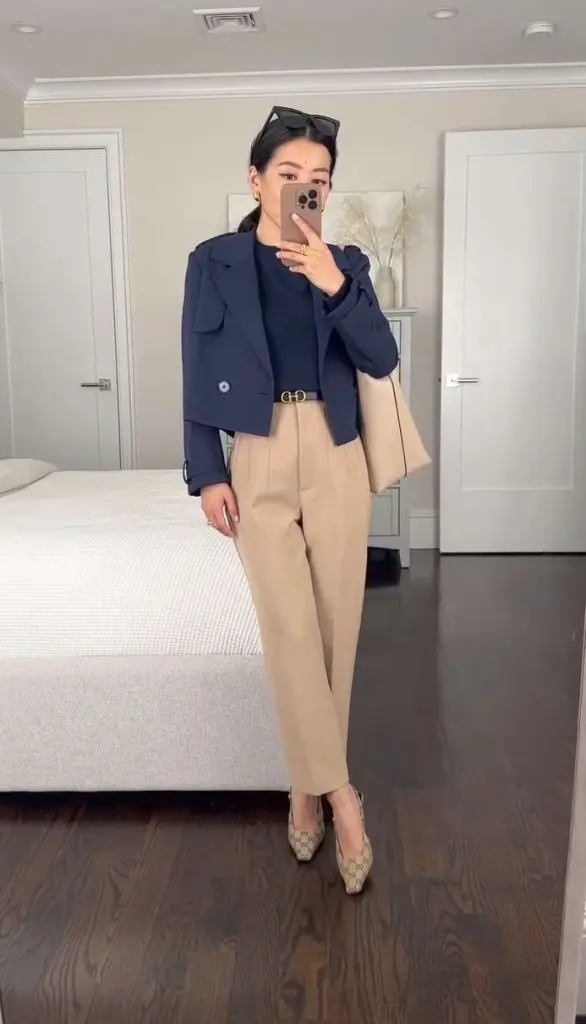 Professional outfit with navy cropped blazer, navy top, beige pleated trousers, designer belt and patterned flats in bedroom setting