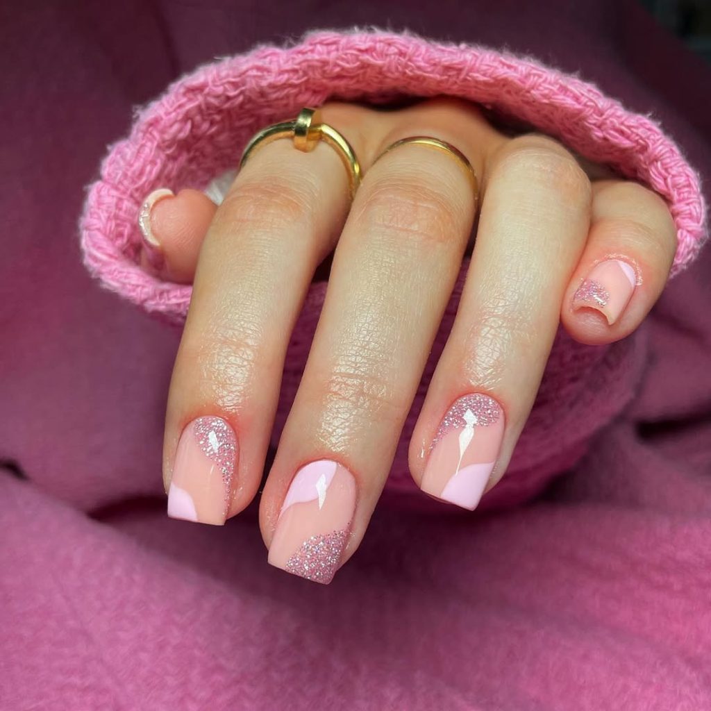 Short square nails with transparent base, diagonal pink polish design and pink glitter accent details 