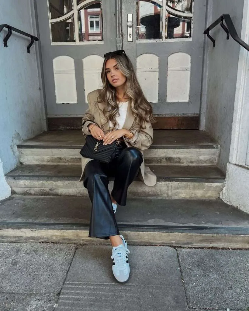 Classy spring outfit with beige oversized coat, white top, black leather trousers, blue sneakers and black Saint Laurent bag
