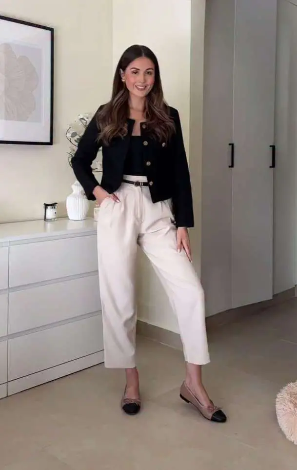 Professional outfit with black cropped jacket, black top, cream wide-leg trousers, thin white belt and beige cap-toe flats in minimalist home setting
