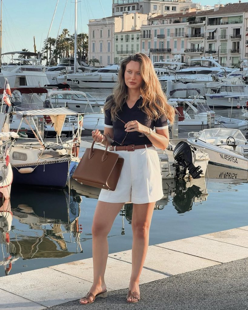 Chic european summer outfit with navy short-sleeve top, white tailored shorts, brown leather sandals, structured brown handbag and sunglasses