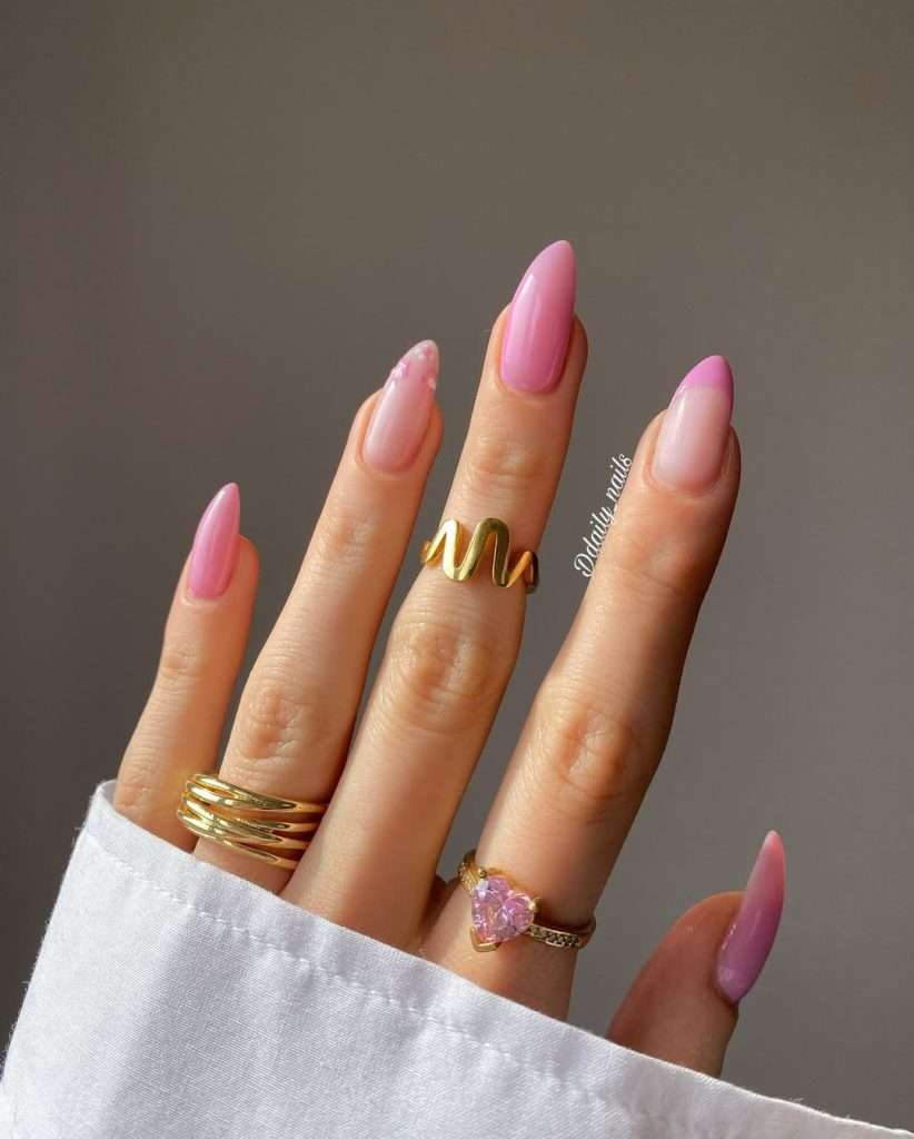 Almond shaped classy nails with three solid pink nails, one pink French tip and one flower accent nail paired with gold rings for elegant spring manicure