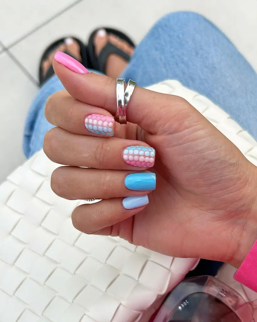 Short summer nails featuring pink and blue polka dot pattern gradient on some nails with solid pink and different shades of blue polish on others