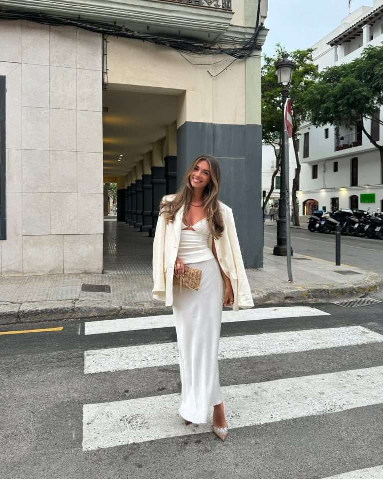 Romantic spring date night outfit with cream blazer, white silky top, matching skirt, straw clutch and sparkly pointed heels