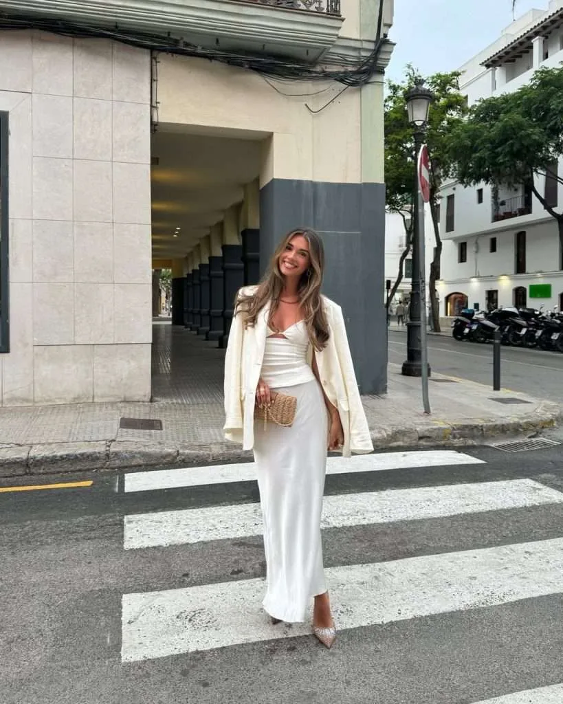 Romantic spring date night outfit with cream blazer, white silky top, matching skirt, straw clutch and sparkly pointed heels
