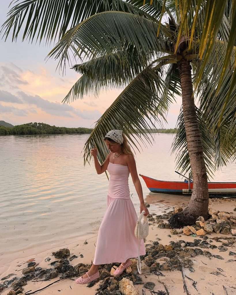Beach vacation outfit with pale pink strapless drop-waist maxi dress, white embroidered headscarf, small white crochet handbag and pink loafers
