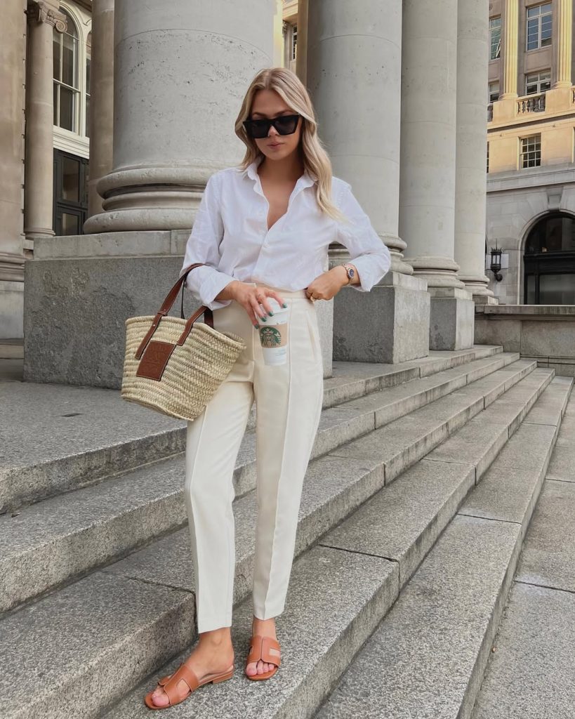 Summer business casual outfit with white button-down shirt, cream tailored trousers, woven straw tote with leather handles, tan leather slide sandals and black rectangular sunglasses