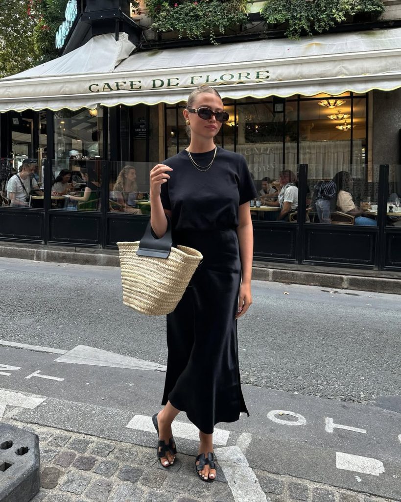 Elegant European vacation outfit with black t-shirt, black silk midi skirt, straw market tote bag and leather sandals
