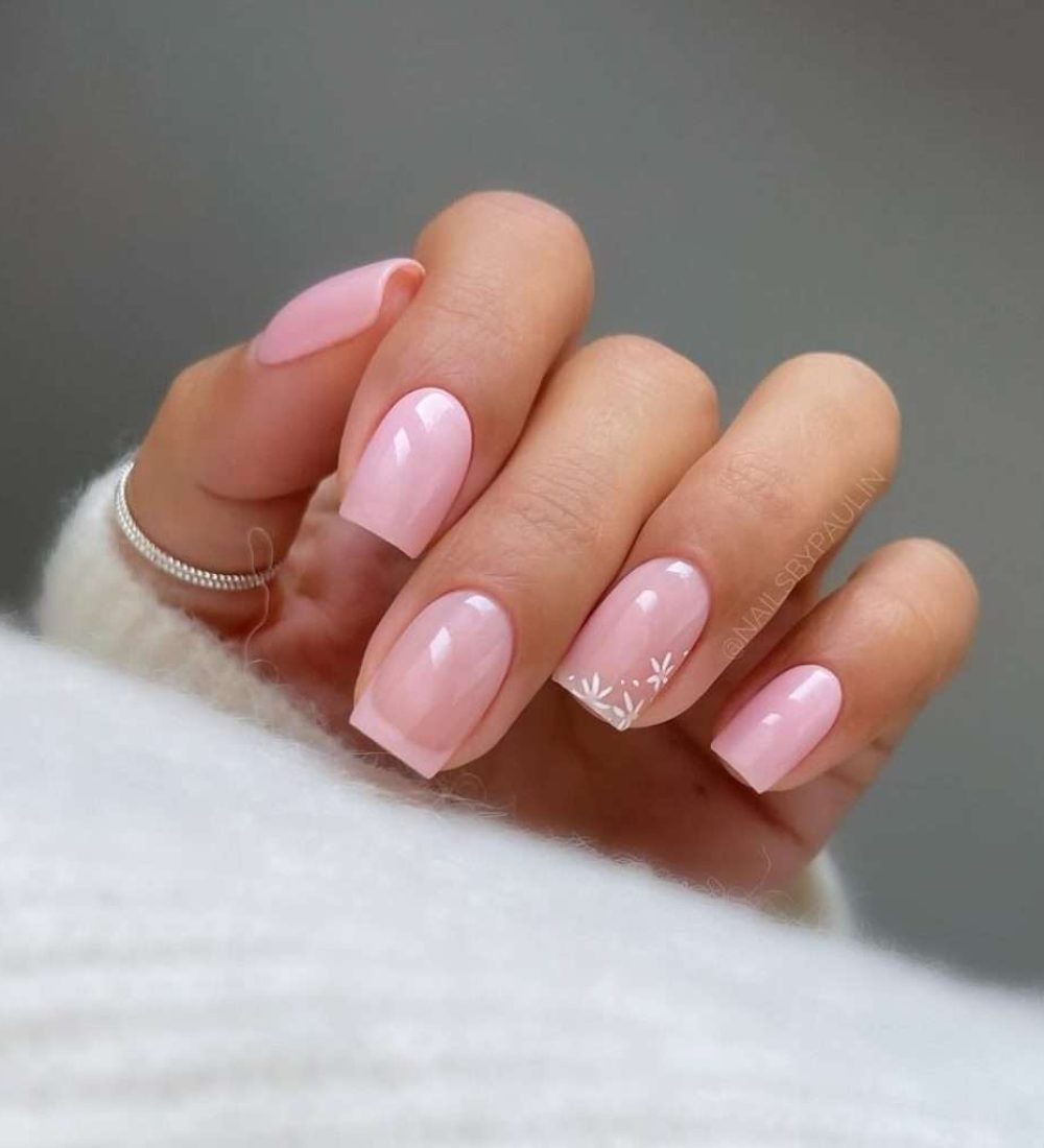 Short square nails in soft pink with white floral French tip accent on one nail