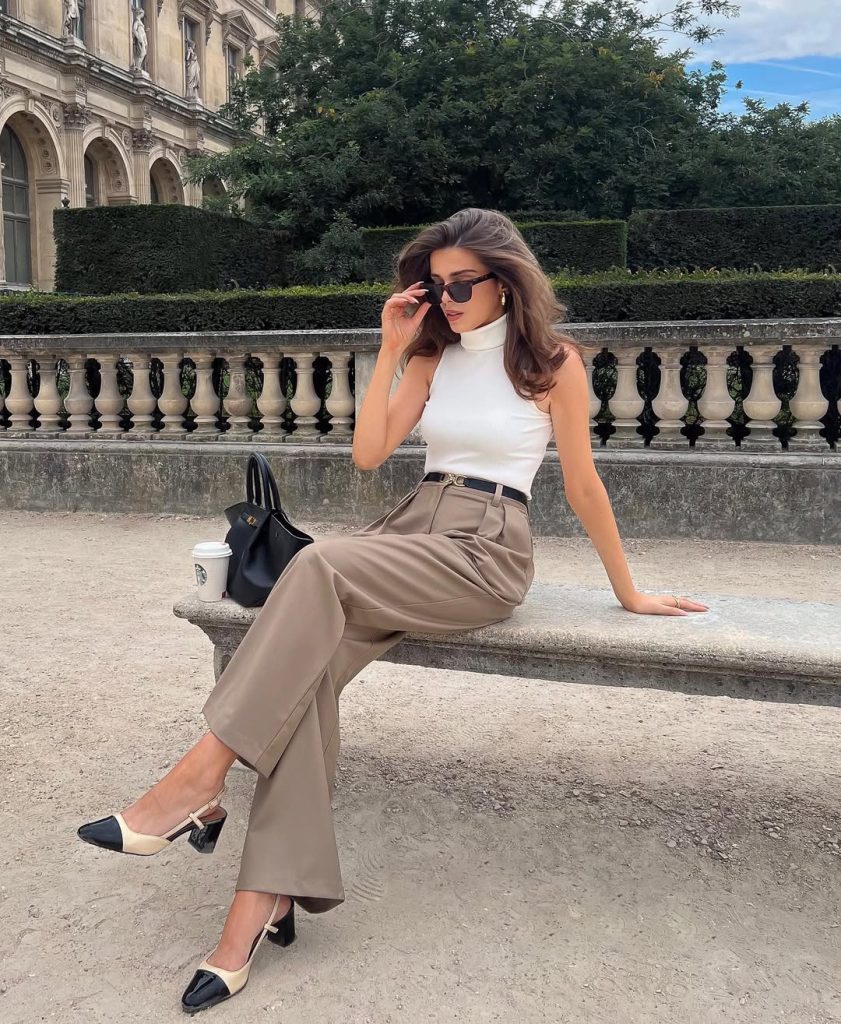 Elegant summer business casual outfit with white sleeveless turtleneck, taupe wide-leg trousers, thin black belt, black structured handbag and beige and black slingback heels
