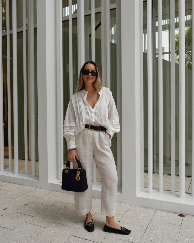 Elegant monochrome outfit with oversized white linen blouse, cream linen pants, brown leather belt, black structured handbag and black loafers with gold hardware