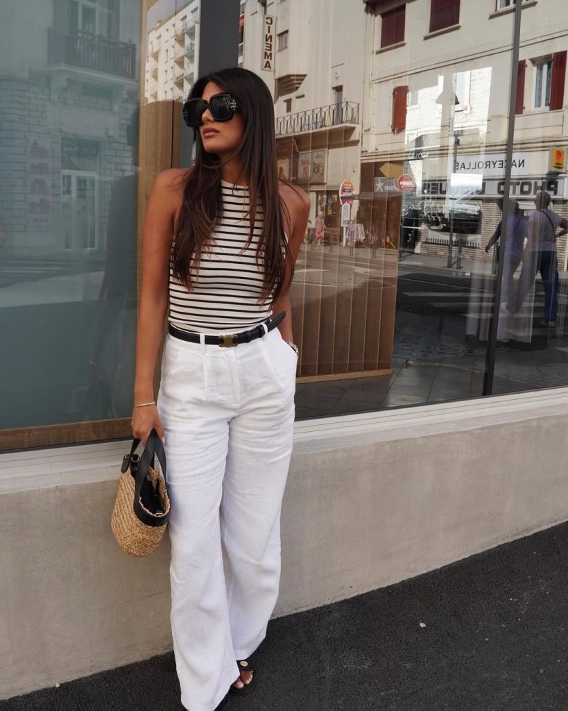 Elegant casual outfit with black and white striped tank top, white wide-leg linen pants, black leather belt, straw basket bag and oversized black sunglasses
