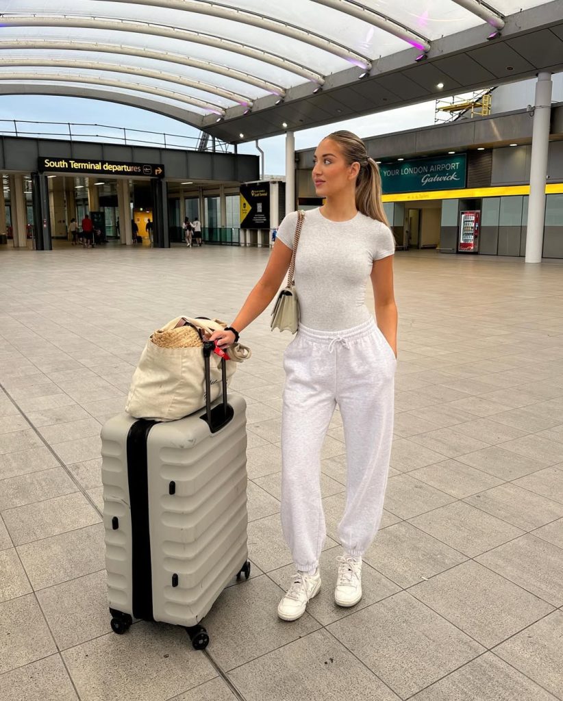 Comfortable airport outfit with fitted white t-shirt, light gray sweatpants, white sneakers, cream crossbody bag and canvas tote at London Gatwick