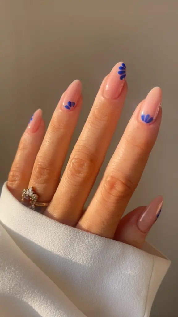 Almond summer nails with sheer pink base and royal blue petal flower designs near cuticles
