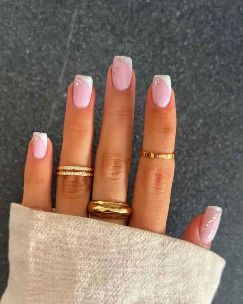 Square pink nails with diagonal white French tips and gold glitter accent lines