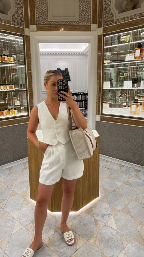 Summer outfit with white tailored vest, matching high-waisted shorts, canvas tote bag and designer white logo slides
