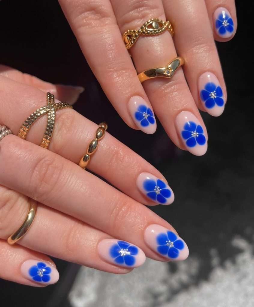 spring almond nails with sheer pink base and bright blue flower design with silver centers

