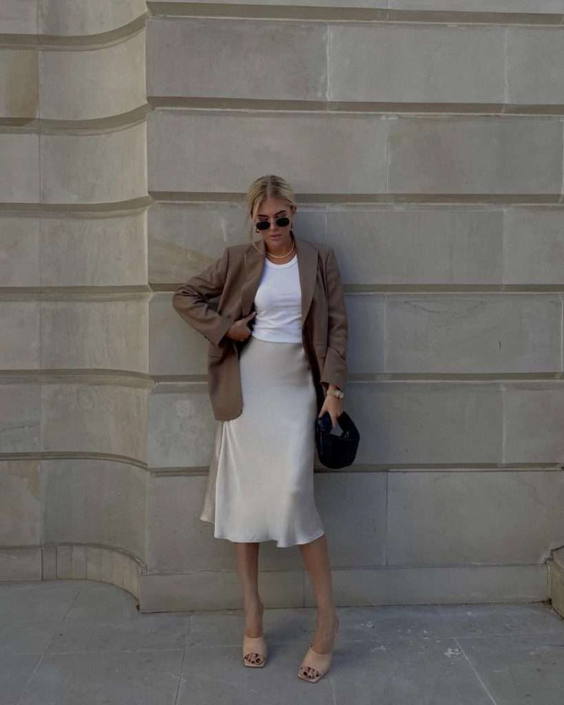 Minimal spring date night outfit with taupe blazer, white crop top, cream silk slip skirt, nude mules and black handbag

