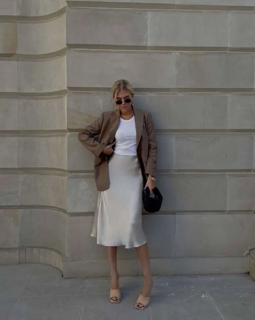 Minimal spring date night outfit with taupe blazer, white crop top, cream silk slip skirt, nude mules and black handbag
