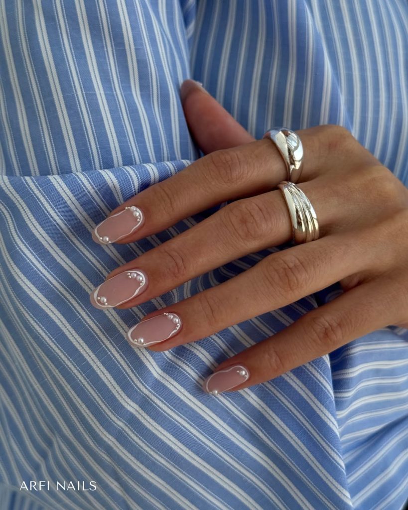 Oval pink nails with thin white borders and pearl accent details
