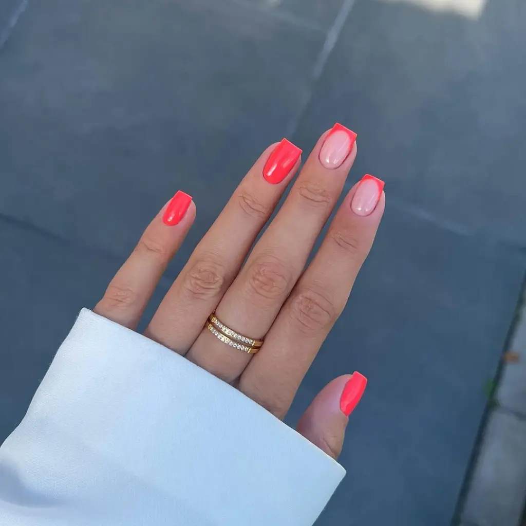 Short square summer nails with alternating bright neon coral polish and transparent pink base with coral French tips